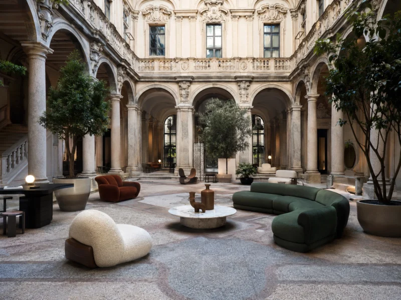 Milan’s design language thrives on contrast, pairing contemporary forms with architecture shaped by centuries. Contemporary furniture displayed within an ornate historic Milanese courtyard